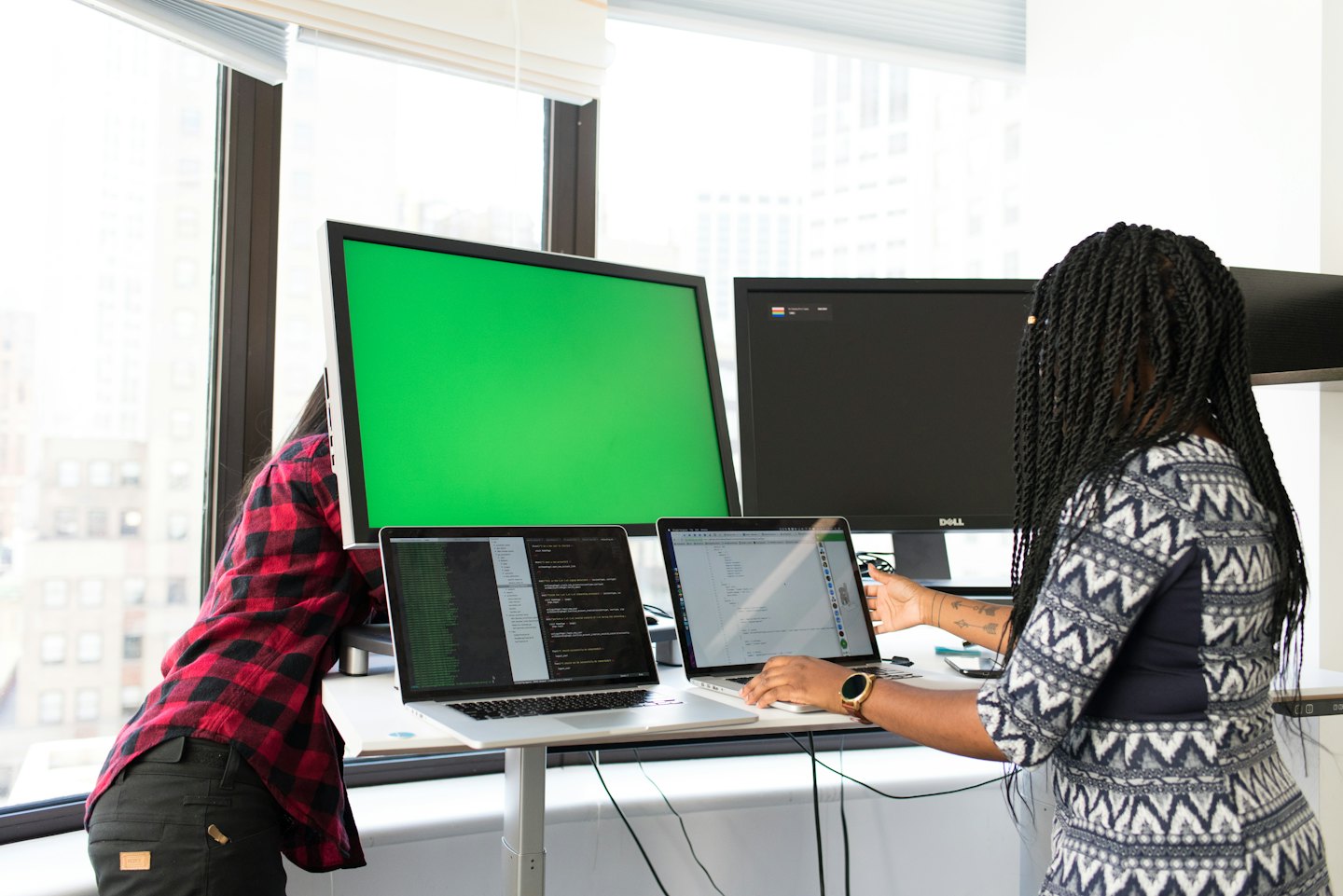 Two people collaborating at an office workstation with coding on screens.