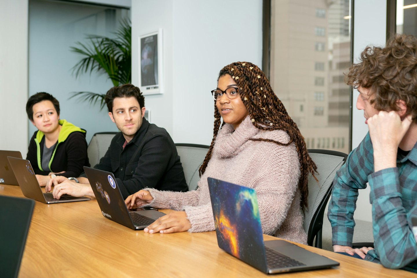 Diverse professionals collaborating around a wooden conference table with laptops.